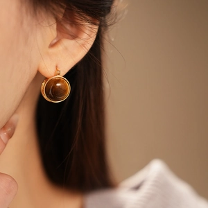Gros plan d'une boucle d'oreille huggie plaquée or avec une pierre œil de tigre ronde sur oreille