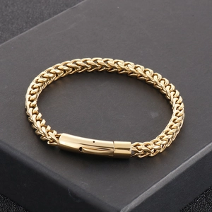 Detalle de una pulsera de acero de titanio trenzado dorado sobre una caja de regalo negra mate