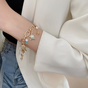 Detail of gold ocean-themed bracelet with turtle, starfish, and pearl charms on a wrist