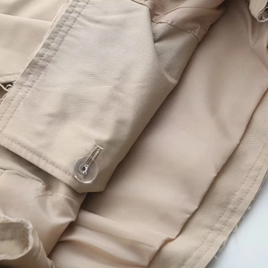 Détail d'un trench-coat kaki montrant un bouton en résine, des coutures et le tissu