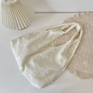 Close-up of white floral embroidery on a cream cotton shoulder bag with knotted handle