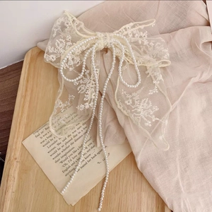 Close-up of beige lace bow hair clip with elegant pearl tassel chains on vintage book
