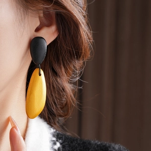 Macro close-up of a model wearing black and yellow drop earrings with matte texture