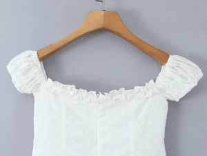Close-up detail of white embroidered blouse featuring puff sleeves and ruffled collar design