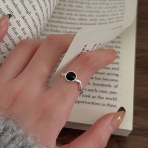 925 sterling silver wavy ring with round black onyx stone on a hand over a book