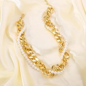 Detail of layered gold metal chains and white faux pearls on champagne silk fabric