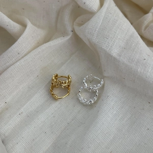 Détail macro de créoles texturées en feuille d'or et d'argent sur tissu en lin beige
