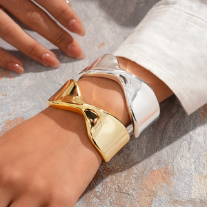 Detail of twisted wide metal cuffs in gold and silver finish on a model's wrist