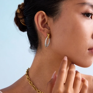 Two-tone oval stud earrings in gold and silver finish worn by a model on blue background