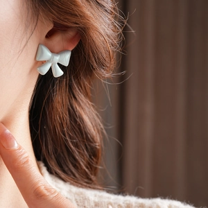 Macro shot of a pearlescent blue bow earring worn by a model in a warm setting