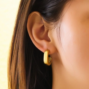 Macro shot of gold-plated chunky U-shaped hoop earrings with a matte brushed finish