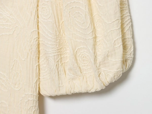 Détail d'une manche bouffante crème avec tissu texturé et broderies en spirale blanche