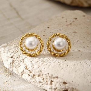Close-up of golden twist hoop earrings with white round pearls on a stone background