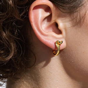 Golden snake hoop earrings with black eye accents worn by a model in a close-up view