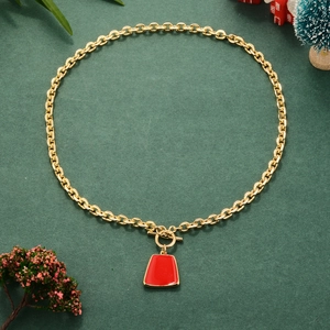 Golden chain necklace with red enamel pendant and OT buckle on a festive green background