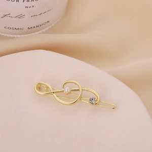 Golden music note hair clip with white pearl and rhinestone on a decorative plate