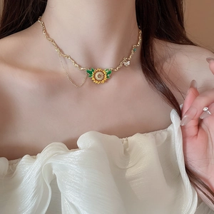 Close-up of a sunflower necklace with bee charm worn on a gold wavy chain