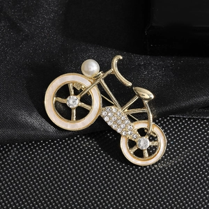 Élégante broche vélo dorée avec cristaux et perle blanche sur fond de tissu noir