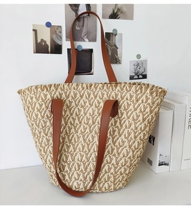 Close-up of the woven paper straw texture and slim brown leather straps on the tote bag