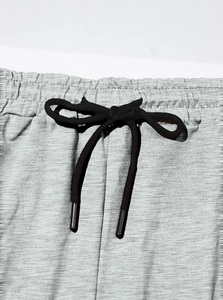 Dettaglio dei pantaloni sportivi grigi con elastico in vita, coulisse nera e trama a nido