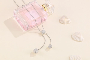 Silver necklace with three crystal-encrusted ball pendants set against shells and perfume