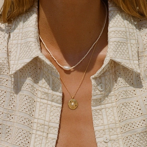Detail of layered gold necklaces with baroque pearls and starburst pendant on model