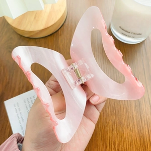 Pink and white marble textured butterfly claw clip for hair styling on a wooden table
