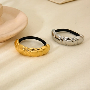 Gold and silver twisted croissant ponytail holders on a minimalist textured background