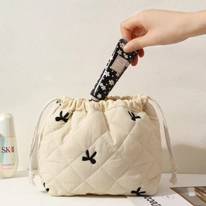 Quilted beige cosmetic pouch with butterfly embroidery being used for skin care storage
