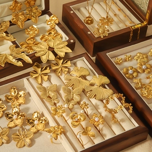 Détail de boucles d'oreilles fleurs et feuilles en or 18k dans des boîtes à bijoux en bois