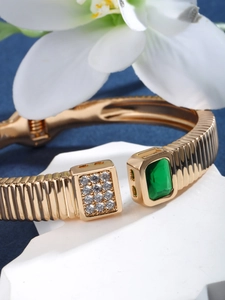 Macro view of a gold-plated luxury hinge bangle with green crystals and small diamonds