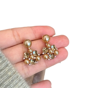 Elegant gold flower drop earrings with pearls and crystals shown on hand in detail