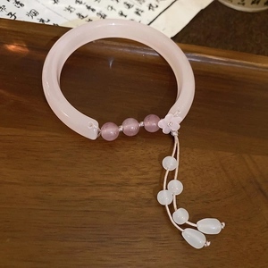 Détail du bracelet en jade rose avec perles violettes et breloques fleuries sur bois