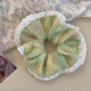 Detail of green plush scrunchie with white lace edges on a minimalist beige surface