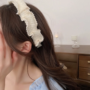 Close-up of cream pleated fabric headband with white pearl trim for an elegant look
