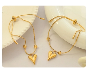 Close-up of gold heart charm bracelet with adjustable drawstring on a ceramic plate