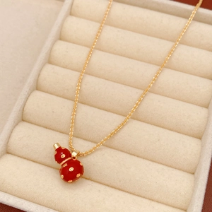 Macro detail of 18k gold plated gourd necklace with red enamel in beige jewelry box