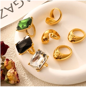 Detail of gold-plated geometric rings with emerald and black gems on white tray
