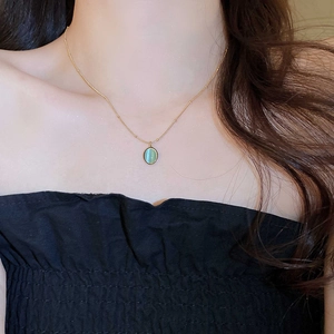 Close-up of a gold necklace featuring a green oval cat-eye stone pendant on model