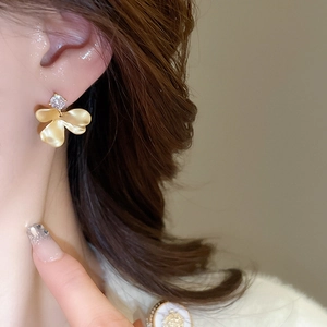 Close-up of elegant gold matte flower earring with sparkling zircon on ear
