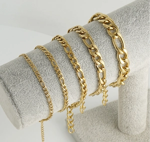 Detalle de cinco anchos de pulseras de cadena Figaro dorada en un soporte gris