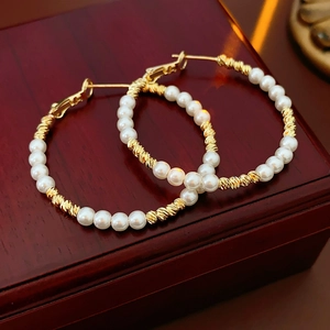 Macro detail of large gold beaded hoop earrings with pearls on a vintage wood box