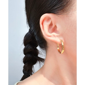Minimalistische unregelmäßige goldene Creolen getragen von einem Modell auf Grau