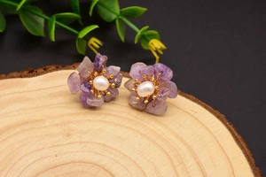 Detailed macro view of a purple stone flower earring with a white pearl on a wood surface