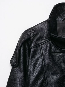 Detail shot of black faux leather jacket featuring stand collar, epaulettes, and pebble texture