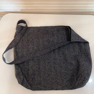 Close-up of the wide shoulder strap and textured dark gray denim fabric of the crossbody bag