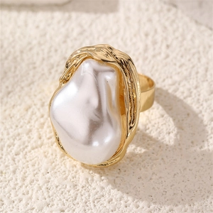 Macro detail of gold-tone cocktail ring with large baroque pearl on white stone surface