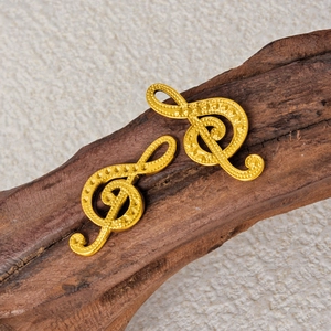 Golden treble clef music note earrings with hammered texture on dark wood background