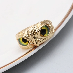 Macro shot of gold owl ring featuring vibrant green eyes and detailed feather texture