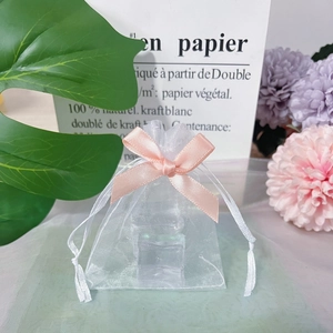 Close-up of white organza gift bag with a pink satin drawstring bow and floral background